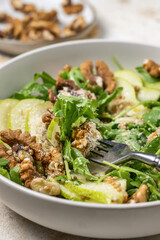 Salad with Pear, Arugula, cheese and walnuts close up. Delicious Fresh Salad on light textured background