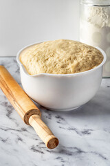 Raw yeast dough in a bowl on white marble background. Making cinnamon rolls. Cinnabon preparation