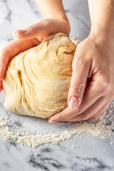 Women's hands kneading dough on white marble table. Making cinnamon rolls process. Cinnabon preparation