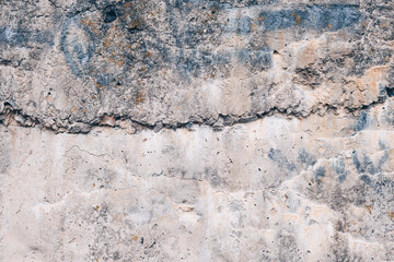 Naklejka premium A fragment of the rough texture of an old concrete surface with cracks, stains and layers of weathered material. Gray-beige shade, pronounced relief and wear. Texture of a concrete wall.