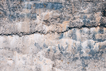 A fragment of the rough texture of an old concrete surface with cracks, stains and layers of weathered material. Gray-beige shade, pronounced relief and wear. Texture of a concrete wall.