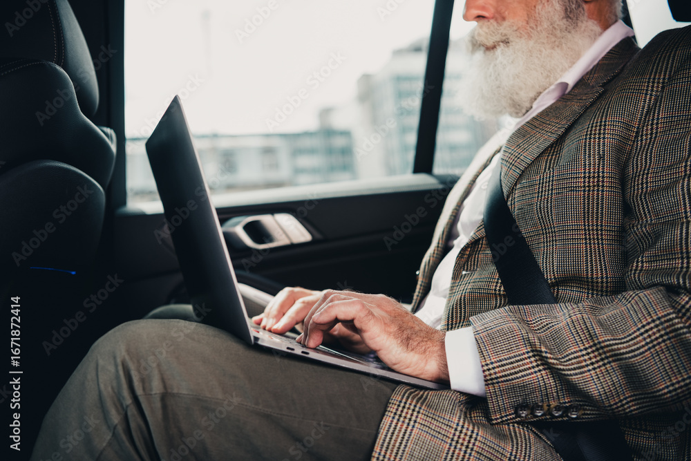 Poster mature man using a laptop in a car displaying a professional demeanor while traveling for work in an