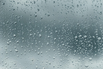 Close-up of raindrops on glass window with cloudy sky in background 