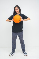 A bold young Asian woman in a full body shot holding a ball firmly in front of her chest with both hands, exuding strength and determination. Isolated on a white background.
