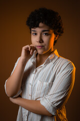 Beautiful young woman with short curly hair, looking at camera with hand on chin. Studio portrait, warm light and copy space. Ideal for Gen Z attitude and contemplation with powerful gaze.