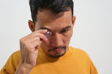 A man carefully uses eye drops or an eye wash solution, focusing on his eye health and personal hygiene routine to maintain clear and comfortable vision.