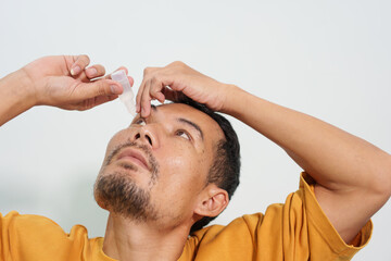 A man carefully uses eye drops or an eye wash solution, focusing on his eye health and personal hygiene routine to maintain clear and comfortable vision.