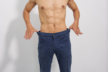 Fototapeta premium A fit man with a toned physique poses confidently in blue jeans, highlighting his healthy lifestyle and casual yet stylish look.