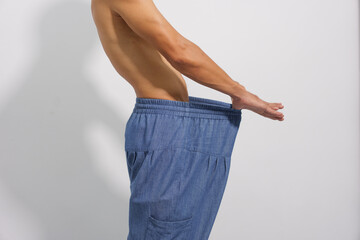 
A fit man with a toned physique shows off his significant weight loss by wearing his old, oversized, and loose denim trousers.