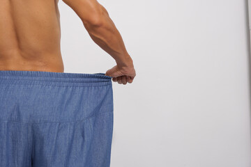 
A fit man with a toned physique shows off his significant weight loss by wearing his old, oversized, and loose denim trousers.