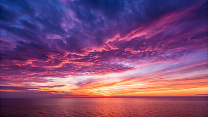 Obraz premium Dramatic sunset sky with fiery orange, pink, and purple clouds over a calm ocean image photo