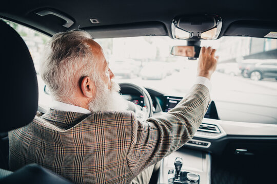 Elegant senior businessman driving in urban traffic, confidently adjusting the rearview mirror, reflecting professionalism