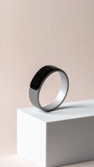 Black and Silver Smart Ring on a White Cube Against a Cream Background Studio Shot