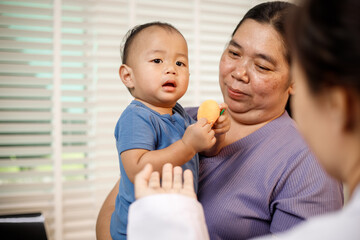 An overweight Asian woman brings her one-year-old son to consult a health expert in a private office. The scene emphasizes family care, professional guidance, wellness improvement