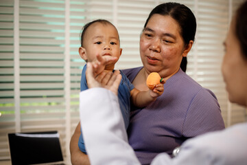 An overweight Asian woman brings her one-year-old son to consult a health expert in a private office. The scene emphasizes family care, professional guidance, wellness improvement
