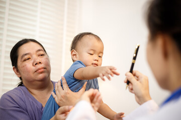 An overweight Asian woman brings her one-year-old son to consult a health expert in a private office. The scene emphasizes family care, professional guidance, wellness improvement