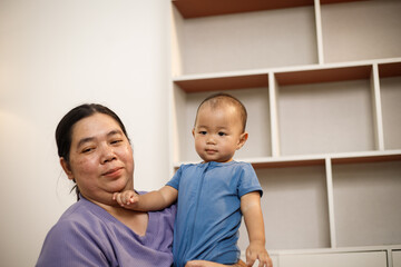 overweight Asian woman joyfully plays with her one-year-old son in a private room, highlighting love, bonding, happiness, and emotional wellness.