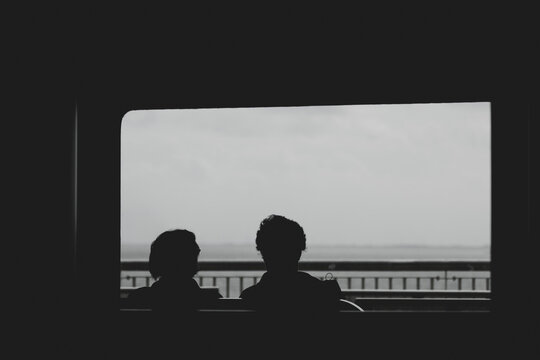 Silhouette of a couple sitting by the window of the ferry looking outside view, Light and shadow of two people in boat with rain and cloudy in dark tone, Blurred passenger in transportation background
