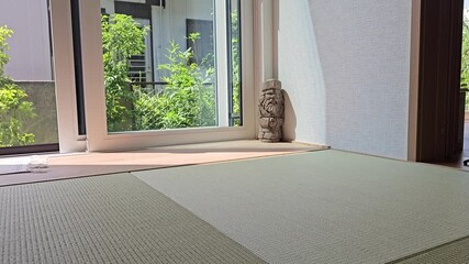 An orange cat crouches on a tatami mat in a Japanese-style room, tail raised and body tense, ready to pounce playfully near a glass door with garden view.