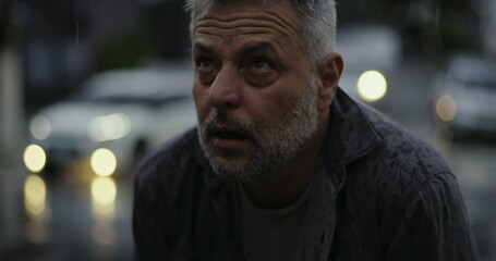 Middle aged man looking upward with raised hands in rain, emotional expression of questioning or...