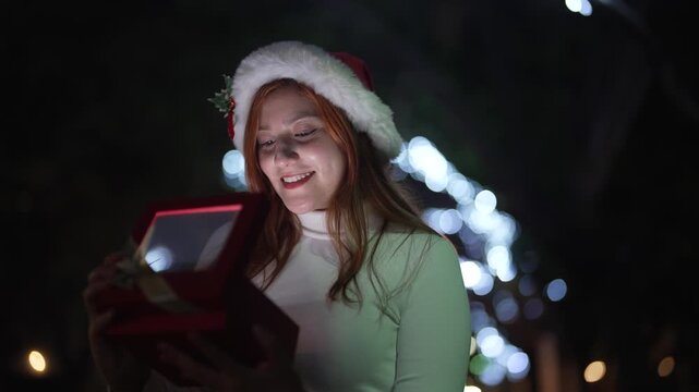 Woman opening glowing Christmas gift box at night with festive lights background