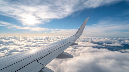 Obraz premium Aerial view of airplane wing above fluffy clouds with bright sun shining in blue sky