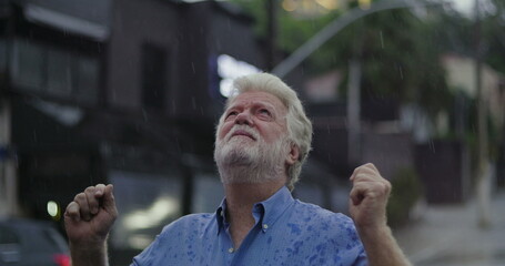 Elderly man standing in the rain, looking upward with open hands and emotional expression of grief,...