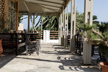 Stock photo of a sunny outdoor restaurant patio with wooden tables, chairs, and a pergola. Perfect for restaurant, travel, or summer themes.