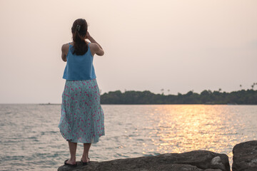 Asian woman standing on rocks looking at sunset over ocean with island in distance