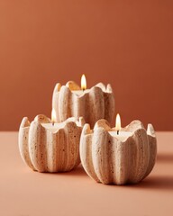 Warm-toned still life of lit travertine candle holders in a minimalist, sculptural style, set against a soft brown background