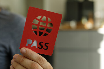 Close-up of a hand holding a red card with a cutout globe and the word PASS.  Perfect for travel,...