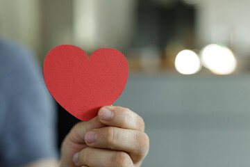Close-up of a hand holding a red paper heart.  Perfect for Valentine's Day, love, and compassion themes.
