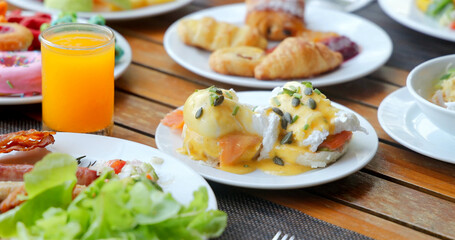 Brunch spread on wooden table with eggs benedict, fresh salad, croissants, donuts, orange juice....