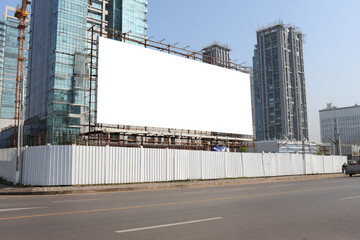 Obraz premium Large blank billboard beside a construction site in a city with modern buildings