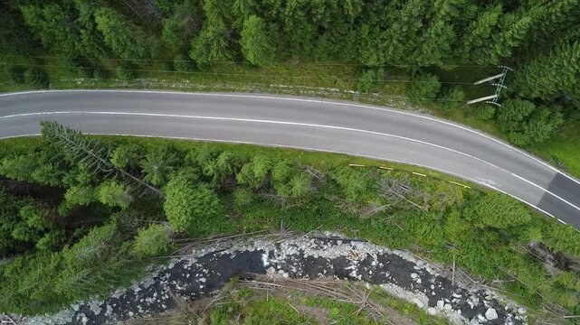 Aerial road curving along forest river with old red-roof building nearby