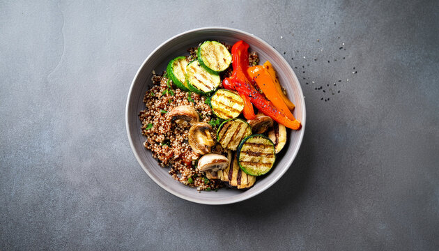overhead shot shows healthy vegan bowl with grilled vegetables and quinoa on a gray surface