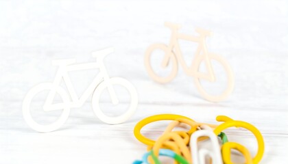 Two small white wooden bicycle models sit on a white wooden surface, near a pile of colorful binder clips