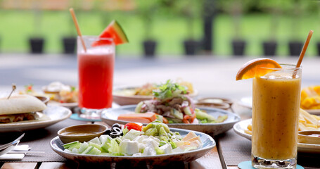 Outdoor dining table with fresh salad, sandwiches, colorful smoothies in garden setting. Healthy...