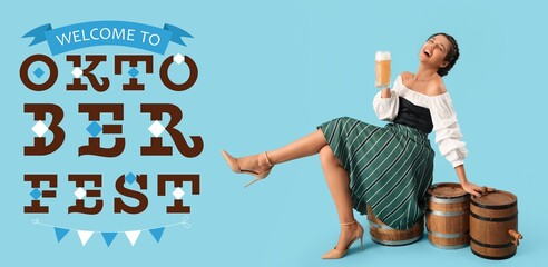 Happy young waitress with beer sitting on barrel against blue background. Octoberfest celebration