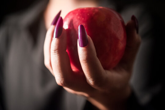 Image of a witch holding an apple in her hand, black background.Close-up.