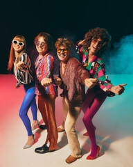 Retro group in bold disco costumes pointing playfully at camera. Concept of vintage lifestyle, pop...