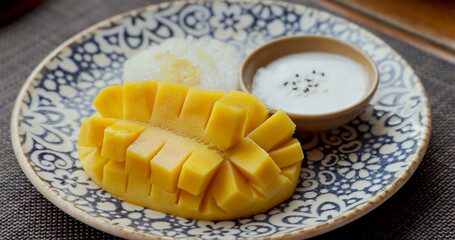 Mango sticky rice dessert on patterned plate, traditional Thai cuisine with ripe mango slices, sweet coconut milk, and sticky rice, exotic Asian Thailand flavor.