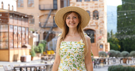 Smiling woman in straw hat standing outdoors in sunny European street, summer travel experience.