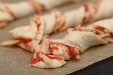 Preparing cheese and ham sticks with tomato sauce for a party, they lie raw on a baking tray