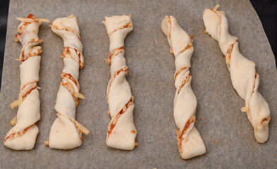 Preparing pizza-flavored twisted sticks from puff pastry, top view of raw sticks lying on baking...