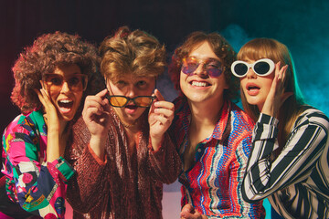 Smiling retro group in bold disco costumes celebrating friendship. Concept of vintage style,...