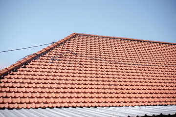 Close-up of a classic red-orange clay tile roof on a house under a clear blue sky. Architectural background of residential roofing material.