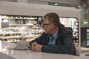 man with glasses sits relaxed at sleek cafe counter. he observes the vibrant atmosphere, surrounded by delicious pastries and drinks. close up.