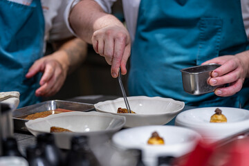 Main d’un chef étoilé en pleine préparation culinaire, dressant un plat gastronomique avec...