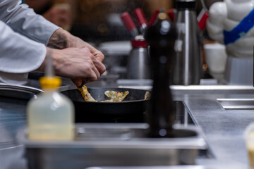 Mains d’un chef en train de faire cuire des langoustines dans une poêle chaude en cuisine professionnelle.